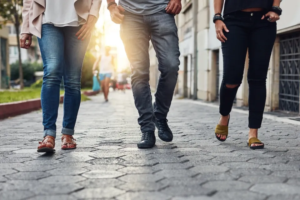 Close-up of bottom half of three people walking down city sidewalk paved with paving stones.